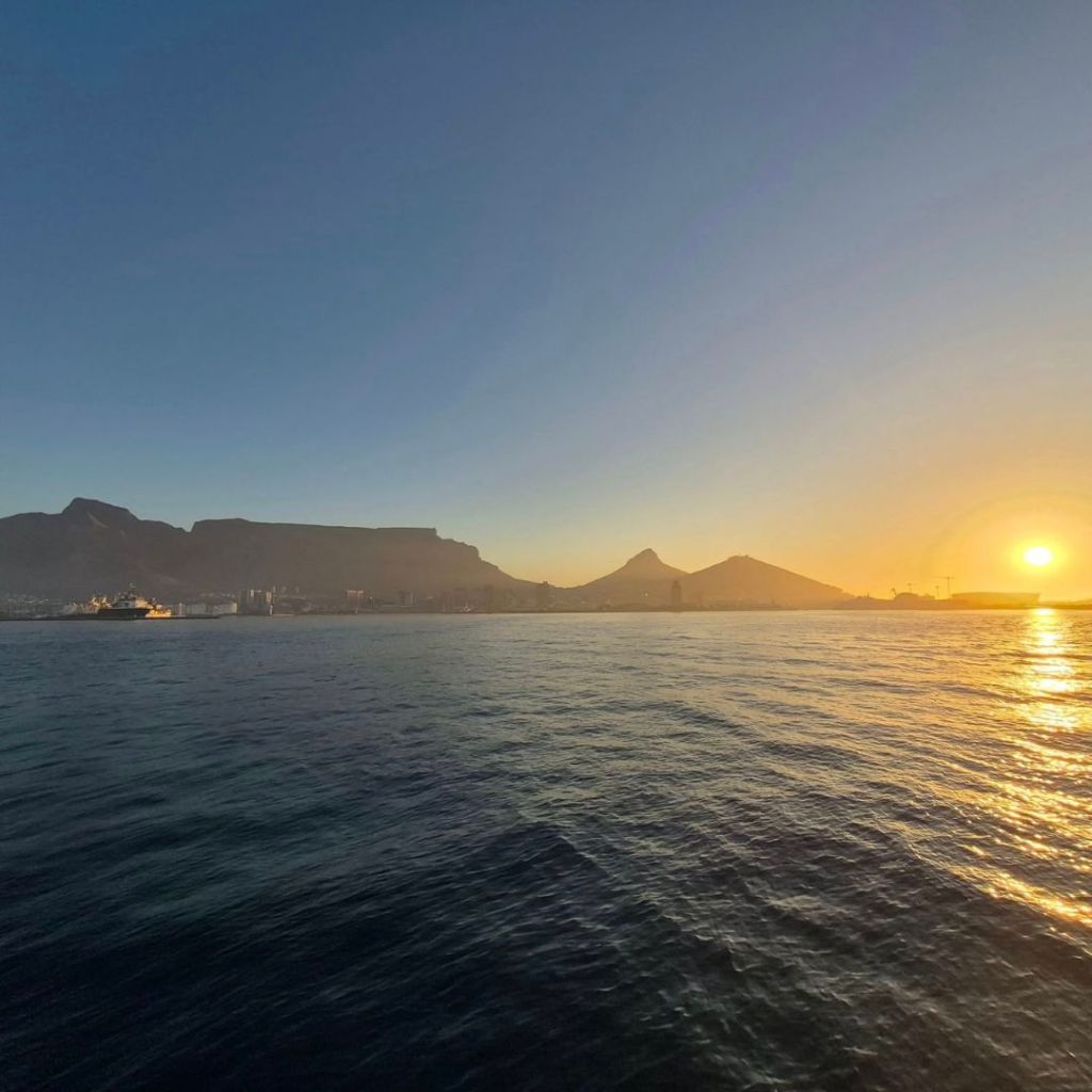 A sunset view over the Atlantic Ocean with silhouettes of Table Mountain and other peaks in Cape Town, South Africa.