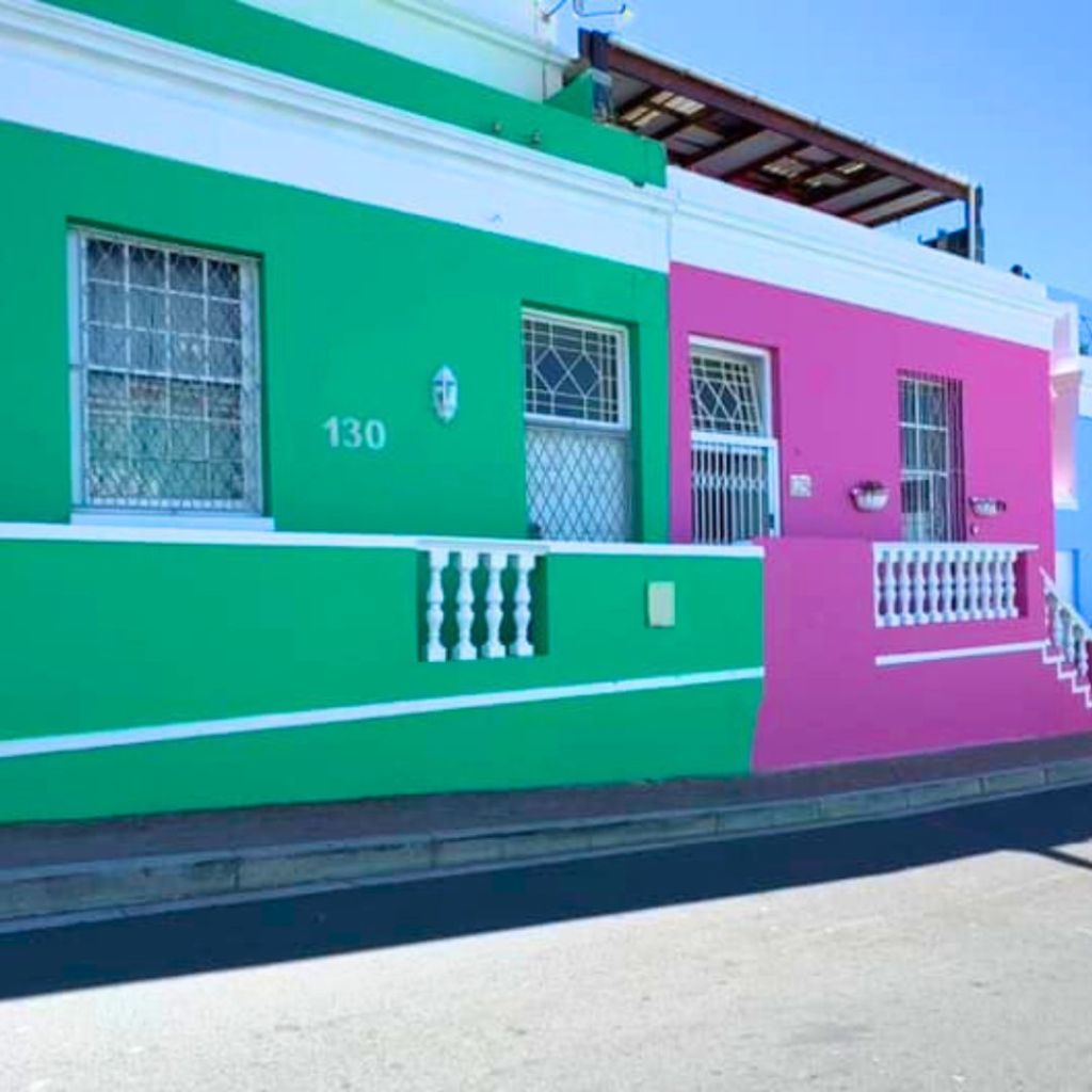 A vibrant photo of a street scene in Bo-Kaap, Cape Town, showcasing a green house next to a pink one, with white trim and decorative features.
