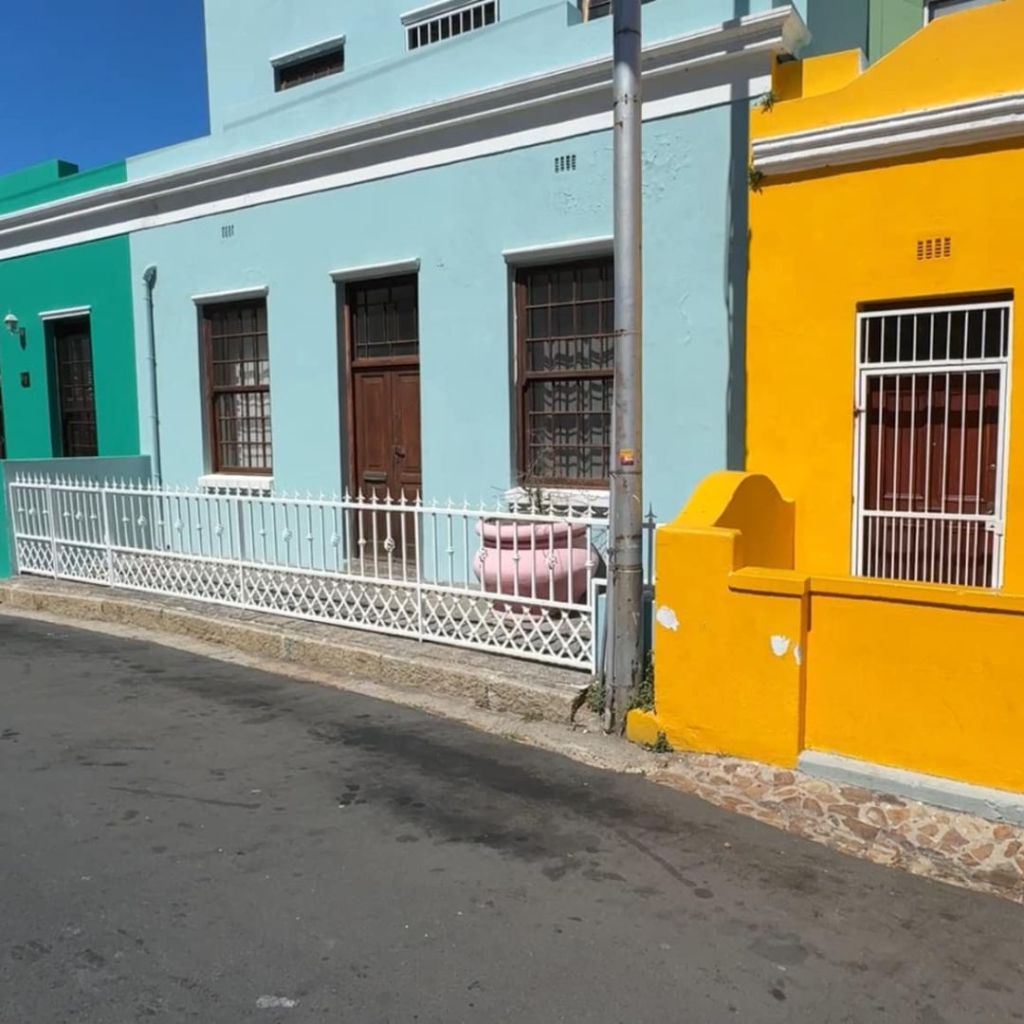 Colorful houses in Cape Town's Bo-Kaap neighborhood, showcasing bright green, blue, yellow, and pink facades along a street with a white fence.