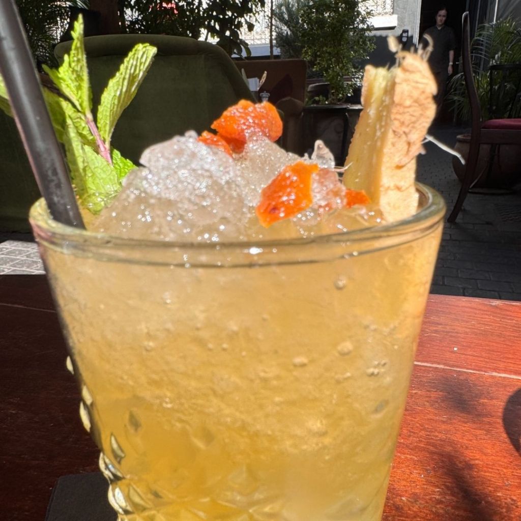 A refreshing cocktail garnished with mint leaves and slices of orange, served in a textured glass on a wooden table.