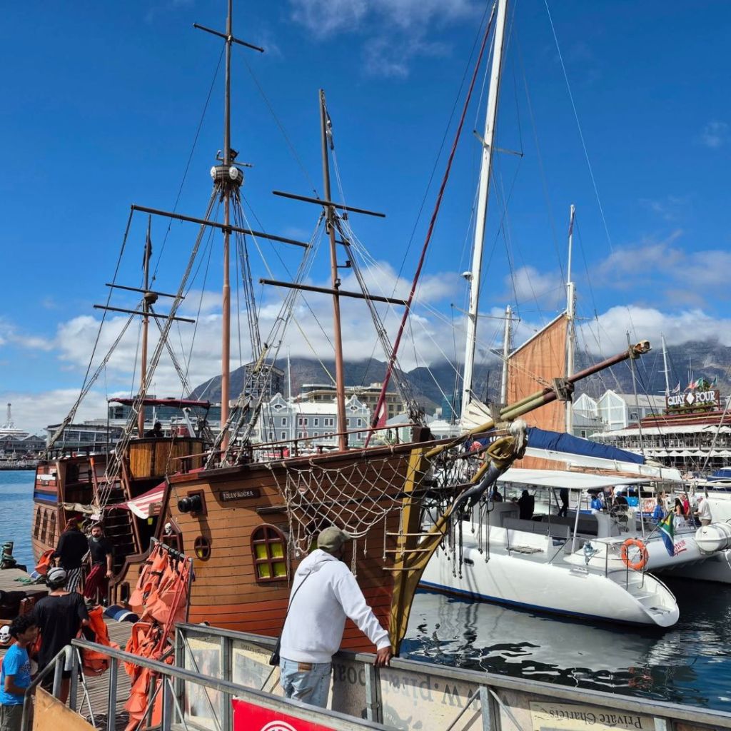 A pirate-themed boat docked at the V&A Waterfront in Cape Town, with a clear blue sky and surrounding sailboats in the background.